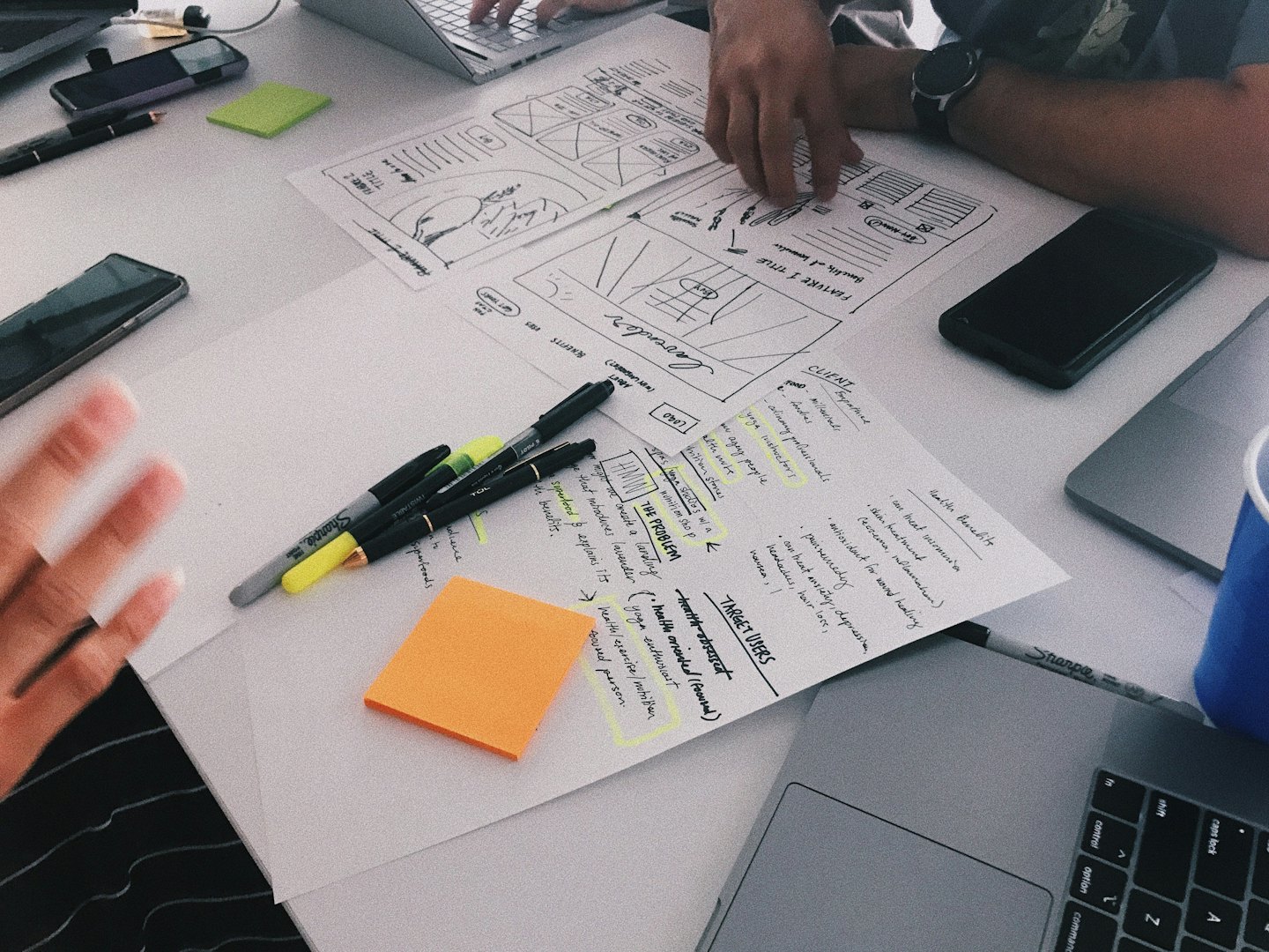 Tre persone collaborano su documenti strategici e laptop a un tavolo bianco.